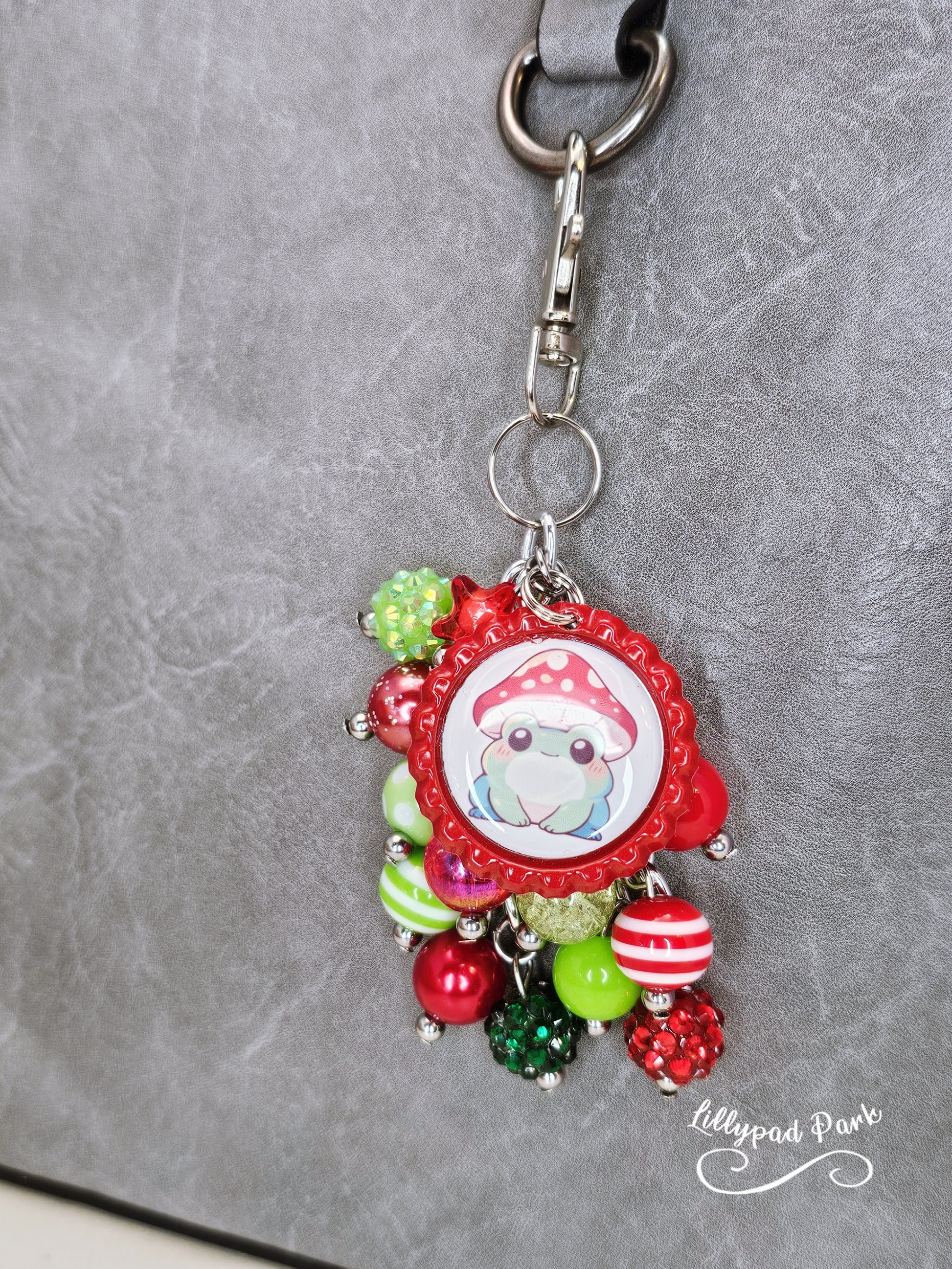 A colorful beaded bag charm featuring a whimsical frog wearing a mushroom cap, with red and green beads and a bottle cap charm.