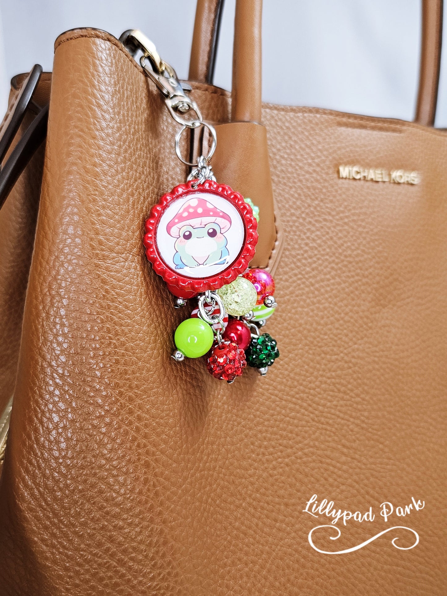 A colorful beaded bag charm featuring a whimsical frog wearing a mushroom cap, with red and green beads and a bottle cap charm.